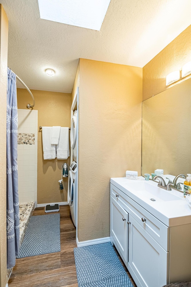 2900 Vista Del Rey NE Unit 18D, Albuquerque, NM 87112 - bathroom featuring stacked washer / drying machine, vanity, wood finished floors, a tile shower, and a textured ceiling