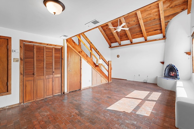 118 Sandia View Rd, Corrales, NM 87048 - unfurnished living room with a warm lit fireplace, a ceiling fan, stairway, and brick floors