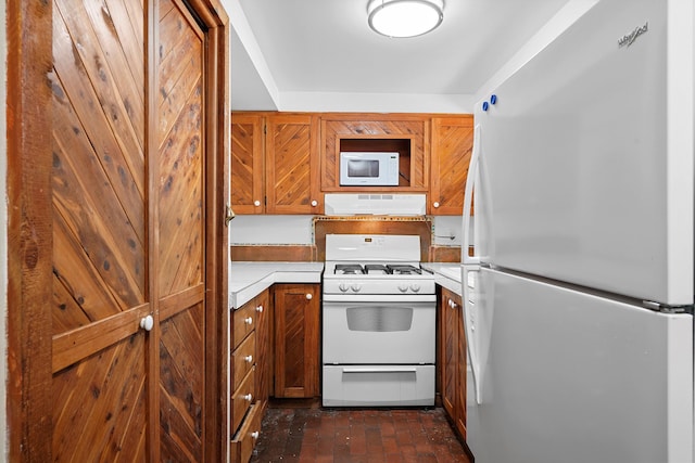 118 Sandia View Rd, Corrales, NM 87048 - kitchen with white appliances, brick floors, under cabinet range hood, light countertops, and brown cabinetry