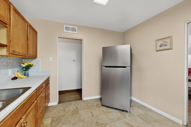 7719 Euclid Ave NE, Albuquerque, NM 87110 - kitchen with freestanding refrigerator, brown cabinetry, light countertops, decorative backsplash, and light tile patterned floors