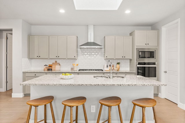 2520 Guadalupe Rd NE, Rio Rancho, NM 87144 - kitchen with wall chimney range hood, appliances with stainless steel finishes, a breakfast bar area, decorative backsplash, and light wood-type flooring