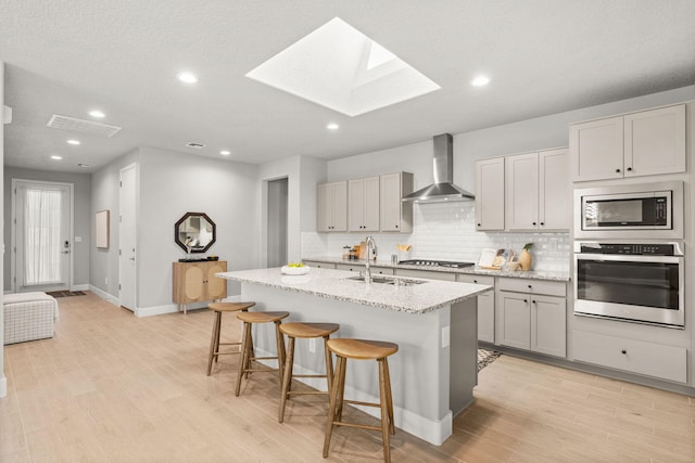 2520 Guadalupe Rd NE, Rio Rancho, NM 87144 - kitchen with stainless steel appliances, wall chimney range hood, a skylight, gray cabinetry, and backsplash