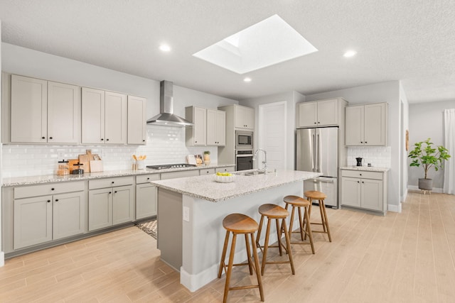 2520 Guadalupe Rd NE, Rio Rancho, NM 87144 - kitchen with wall chimney exhaust hood, stainless steel appliances, a skylight, a kitchen breakfast bar, and light wood-type flooring