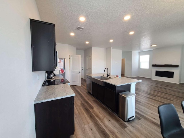 4300 Lauren NE, Rio Rancho, NM 87124 - kitchen with dark cabinetry, a textured ceiling, appliances with stainless steel finishes, an island with sink, and wood finished floors