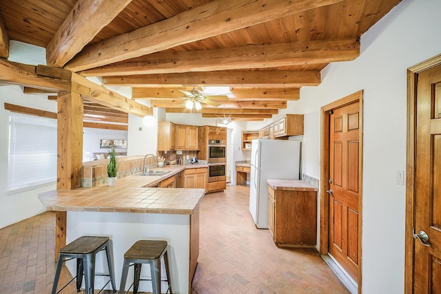 2505 Elfego Rd NW, Albuquerque, NM 87107 - kitchen featuring freestanding refrigerator, brick floors, tile counters, a peninsula, and a wood ceiling with exposed beams