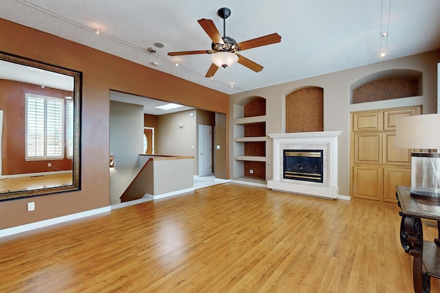 4104 Killington Rd NW, Albuquerque, NM 87114 - unfurnished living room featuring built in features, light wood-style flooring, a ceiling fan, and a glass covered fireplace