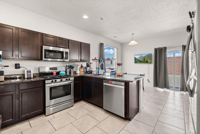 9909 Saddlehorn Trl SW, Albuquerque, NM 87121 - kitchen featuring appliances with stainless steel finishes, dark brown cabinetry, a peninsula, a textured ceiling, and dark stone countertops