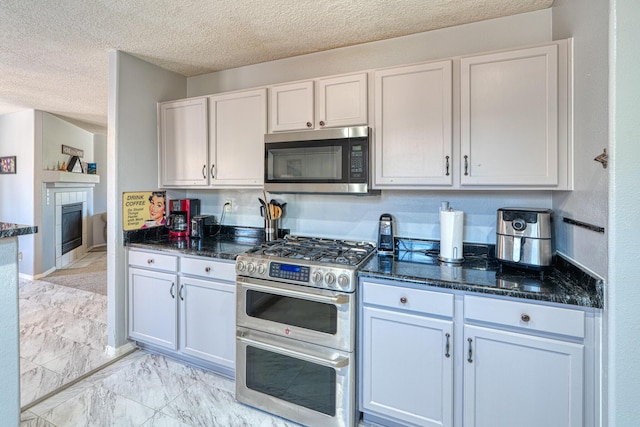 10405 Red Robin Rd SW, Albuquerque, NM 87121 - kitchen with stainless steel appliances, dark stone counters, light marble finish flooring, a tiled fireplace, and a textured ceiling