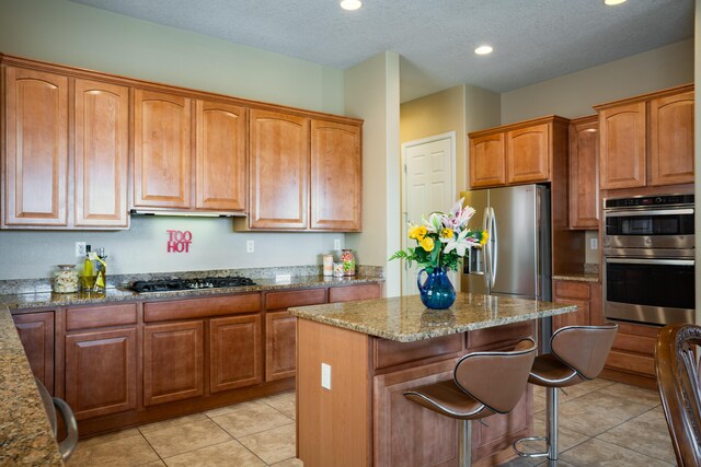 3726 Linda Vista Ave NE, Rio Rancho, NM 87124 - kitchen featuring appliances with stainless steel finishes, stone counters, a kitchen island, light tile patterned floors, and a breakfast bar area