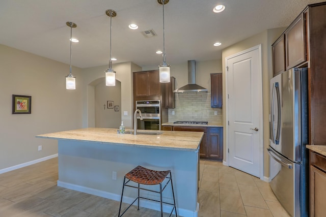 2952 Kings Canyon Loop NE, Rio Rancho, NM 87144 - kitchen with stainless steel appliances, wall chimney range hood, arched walkways, decorative backsplash, and a center island with sink