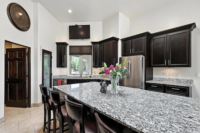 76 Otero Rd, Los Lunas, NM 87031 - kitchen featuring stainless steel refrigerator with ice dispenser, light stone counters, a kitchen breakfast bar, light tile patterned floors, and dark cabinets