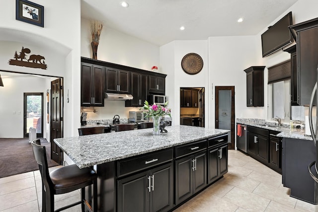 76 Otero Rd, Los Lunas, NM 87031 - kitchen with a center island, light tile patterned floors, under cabinet range hood, light stone counters, and a towering ceiling