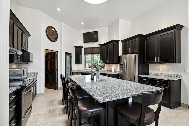 76 Otero Rd, Los Lunas, NM 87031 - kitchen featuring appliances with stainless steel finishes, a kitchen island, a kitchen bar, a high ceiling, and light stone counters
