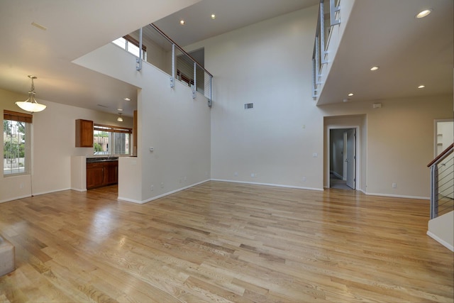 315 11th St SW, Albuquerque, NM 87102 - unfurnished living room with stairway, a towering ceiling, light wood-style flooring, and recessed lighting
