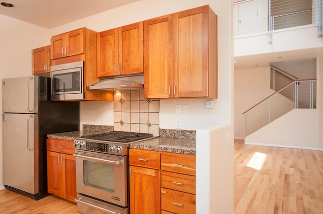 315 11th St SW, Albuquerque, NM 87102 - kitchen featuring appliances with stainless steel finishes, under cabinet range hood, light wood-style flooring, backsplash, and brown cabinetry