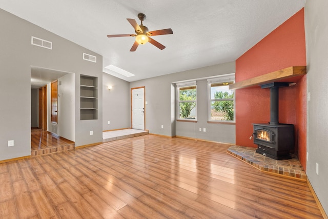 36 Palomas Rd, Los Lunas, NM 87031 - unfurnished living room featuring a ceiling fan, built in features, light wood-type flooring, a wood stove, and vaulted ceiling