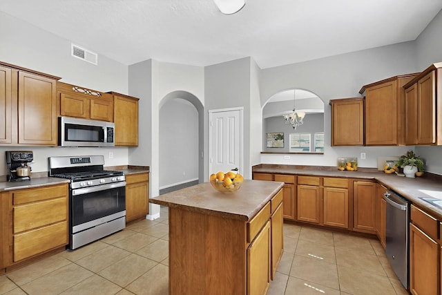 2048 N Ensenada Cir SE, Rio Rancho, NM 87124 - kitchen featuring appliances with stainless steel finishes, arched walkways, a chandelier, a kitchen island, and brown cabinets