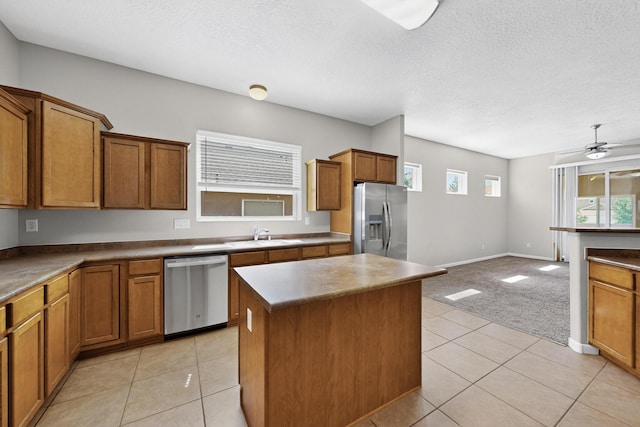 2048 N Ensenada Cir SE, Rio Rancho, NM 87124 - kitchen with stainless steel appliances, brown cabinetry, a kitchen island, a ceiling fan, and light tile patterned flooring