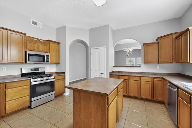 2048 N Ensenada Cir SE, Rio Rancho, NM 87124 - kitchen featuring stainless steel appliances, arched walkways, a center island, a chandelier, and brown cabinetry