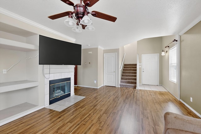 701 Autumn Meadows Dr, Rio Rancho, NM 87144 - unfurnished living room featuring light wood-style flooring, a ceiling fan, stairs, a tile fireplace, and ornamental molding