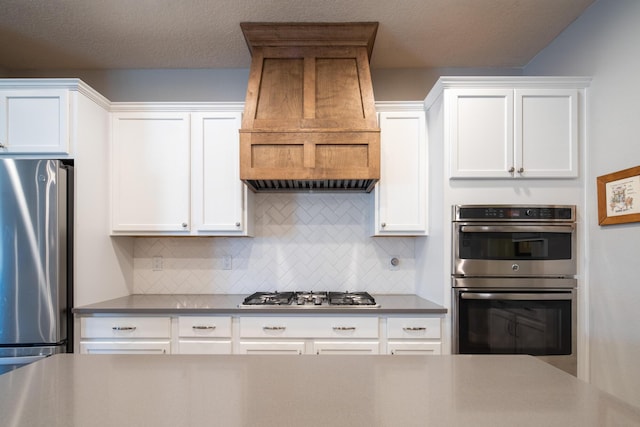 1978 Castle Peak Loop NE, Rio Rancho, NM 87144 - kitchen featuring appliances with stainless steel finishes, premium range hood, tasteful backsplash, white cabinets, and a textured ceiling