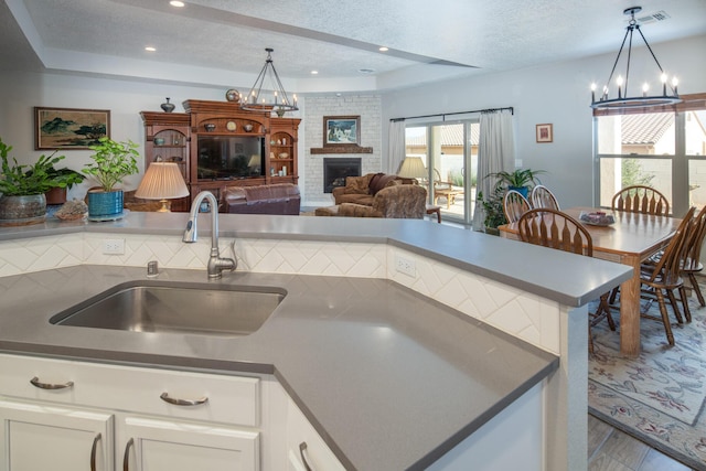 1978 Castle Peak Loop NE, Rio Rancho, NM 87144 - kitchen with a chandelier, a fireplace, wood finished floors, white cabinetry, and hanging light fixtures