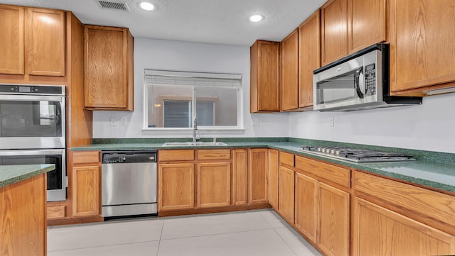 3536 Clear Creek Pl, Rio Rancho, NM 87144 - kitchen featuring stainless steel appliances, light tile patterned floors, dark countertops, recessed lighting, and brown cabinetry