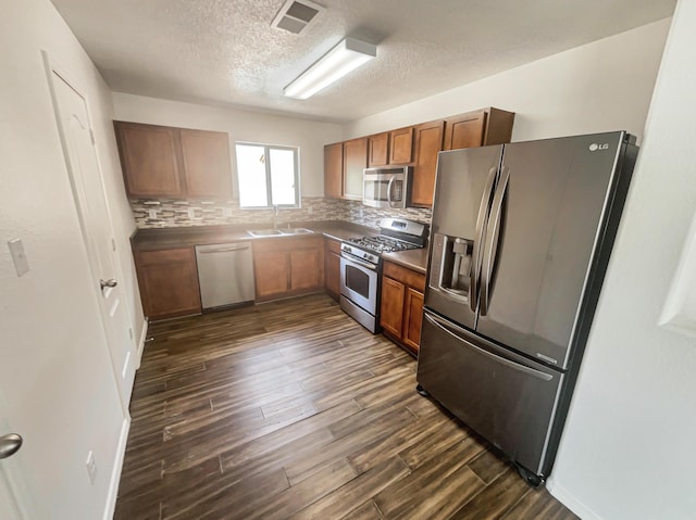 1225 La Fonda St, Bernalillo, NM 87004 - kitchen with stainless steel appliances, a textured ceiling, dark wood-style flooring, backsplash, and brown cabinets