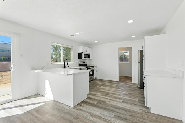 9638 Morrow Ave NE, Albuquerque, NM 87112 - kitchen with stainless steel appliances, light wood-style floors, white cabinets, a peninsula, and light countertops