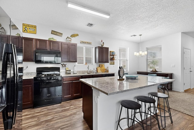 6383 Gannett Dr NE, Rio Rancho, NM 87144 - kitchen featuring black appliances, light wood finished floors, a chandelier, a kitchen bar, and a center island