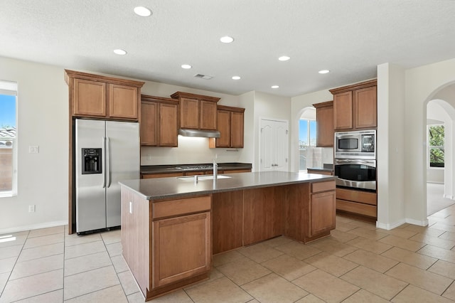 6903 Wrangell Loop NE, Rio Rancho, NM 87144 - kitchen with appliances with stainless steel finishes, arched walkways, under cabinet range hood, a kitchen island with sink, and brown cabinetry