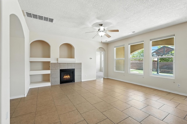 6903 Wrangell Loop NE, Rio Rancho, NM 87144 - unfurnished living room featuring built in shelves, a textured ceiling, tile patterned flooring, ceiling fan, and a fireplace