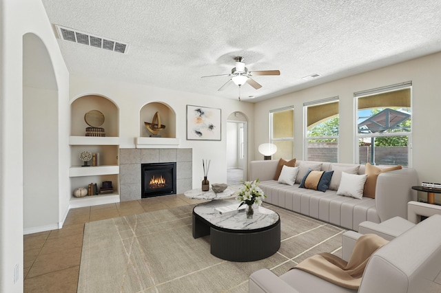 6903 Wrangell Loop NE, Rio Rancho, NM 87144 - living room with built in shelves, a tile fireplace, a ceiling fan, tile patterned flooring, and a textured ceiling
