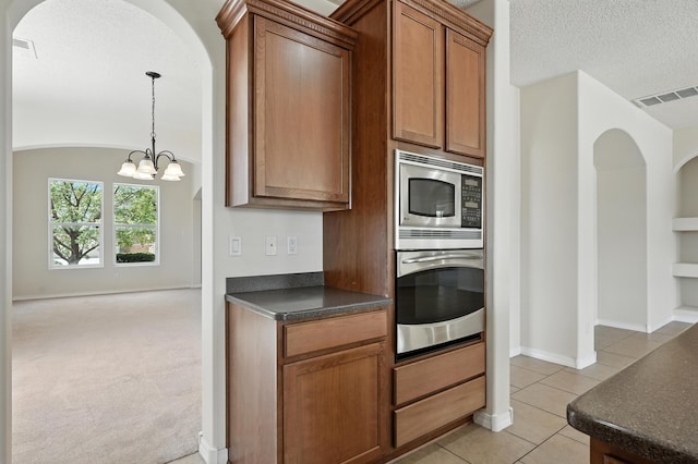 6903 Wrangell Loop NE, Rio Rancho, NM 87144 - kitchen with stainless steel appliances, dark countertops, arched walkways, light tile patterned flooring, and brown cabinets
