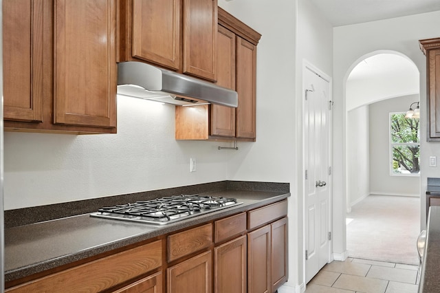6903 Wrangell Loop NE, Rio Rancho, NM 87144 - kitchen featuring under cabinet range hood, stainless steel gas stovetop, dark countertops, brown cabinets, and arched walkways