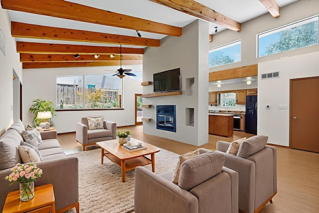 1865 Tramway Terrace Loop NE, Albuquerque, NM 87122 - living area with a high ceiling, beam ceiling, a glass covered fireplace, a ceiling fan, and light wood-style floors