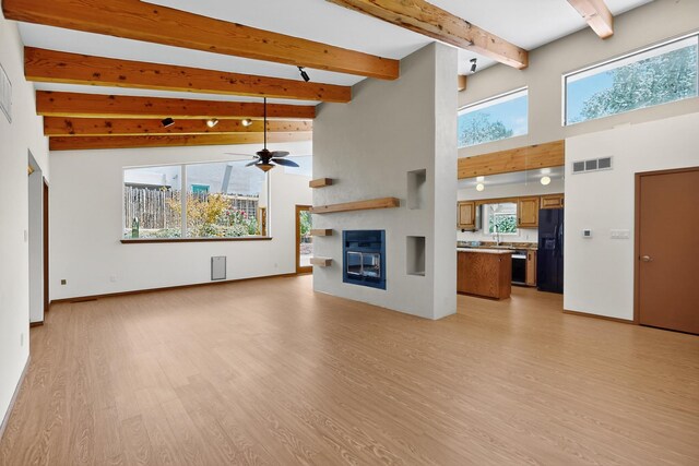 1865 Tramway Terrace Loop NE, Albuquerque, NM 87122 - unfurnished living room featuring a towering ceiling, light wood finished floors, ceiling fan, beam ceiling, and a glass covered fireplace