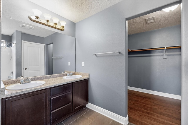 1324 Desert Paintbrush Loop, Rio Rancho, NM 87144 - bathroom featuring a textured ceiling, double vanity, a walk in closet, and wood finished floors