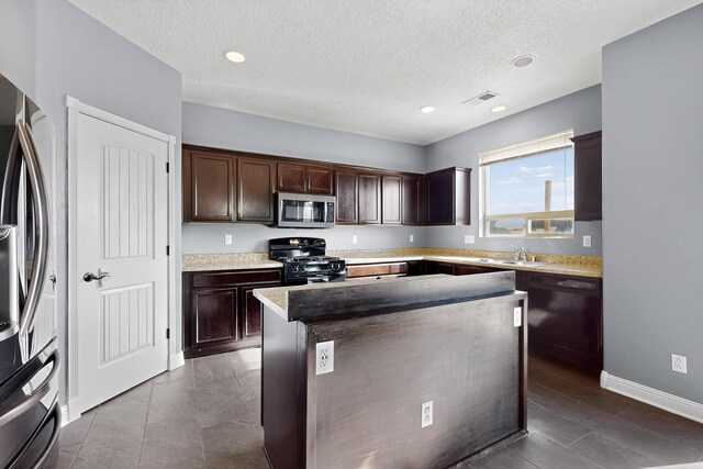 1324 Desert Paintbrush Loop, Rio Rancho, NM 87144 - kitchen with stainless steel appliances, dark brown cabinetry, a textured ceiling, a kitchen island, and light countertops
