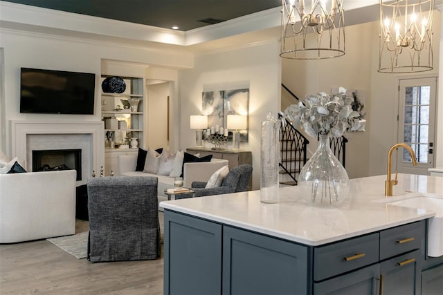 kitchen featuring light wood-type flooring, a kitchen island, sink, a tray ceiling, and crown molding