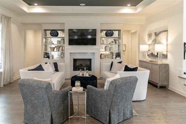 living room featuring light hardwood / wood-style flooring, built in shelves, a fireplace, a raised ceiling, and ornamental molding