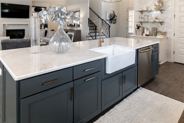 kitchen featuring a high end fireplace, an island with sink, stainless steel dishwasher, sink, and dark hardwood / wood-style floors