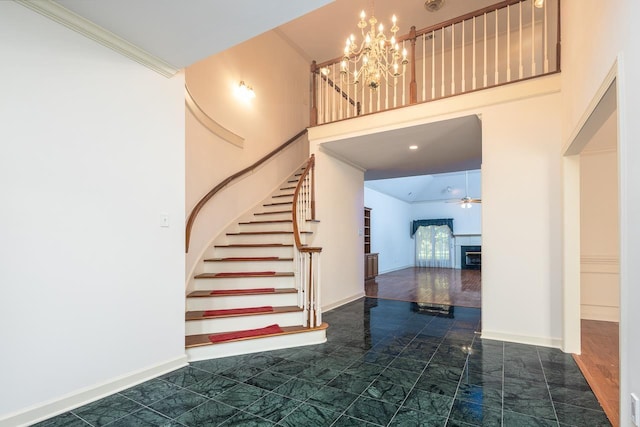 staircase featuring ornamental molding, ceiling fan with notable chandelier, and dark tile floors