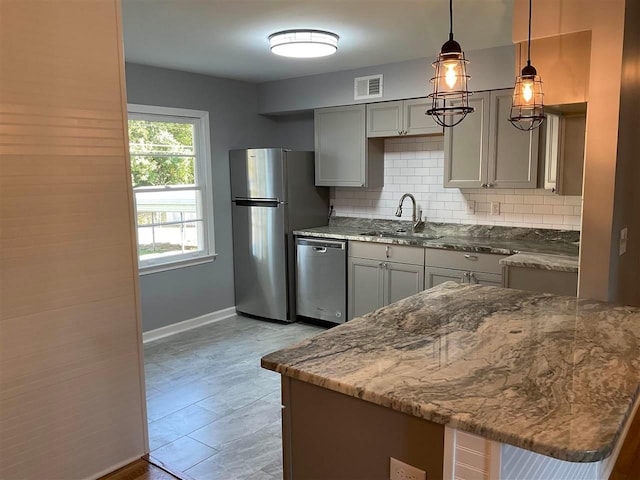 kitchen featuring appliances with stainless steel finishes, light stone counters, pendant lighting, backsplash, and sink