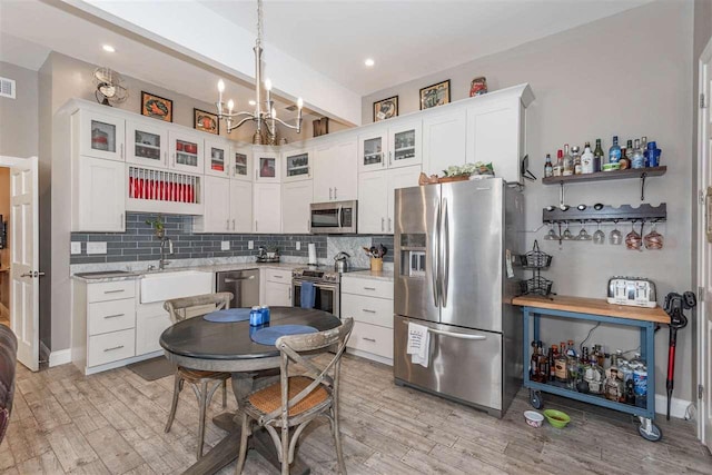 kitchen with appliances with stainless steel finishes, sink, white cabinets, a chandelier, and tasteful backsplash