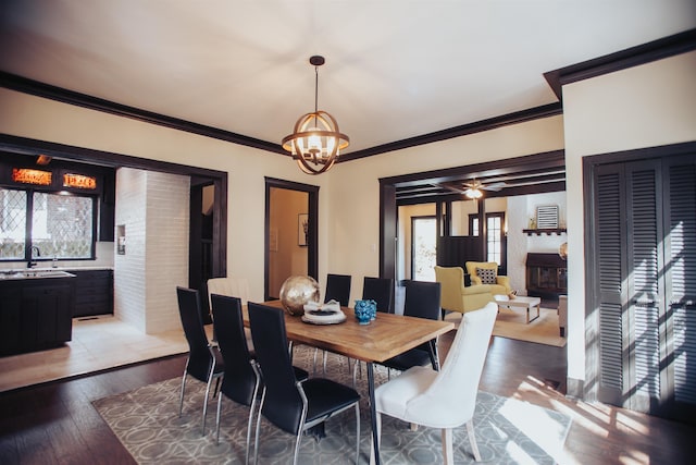 dining space with light tile flooring, a fireplace, ceiling fan with notable chandelier, sink, and ornamental molding