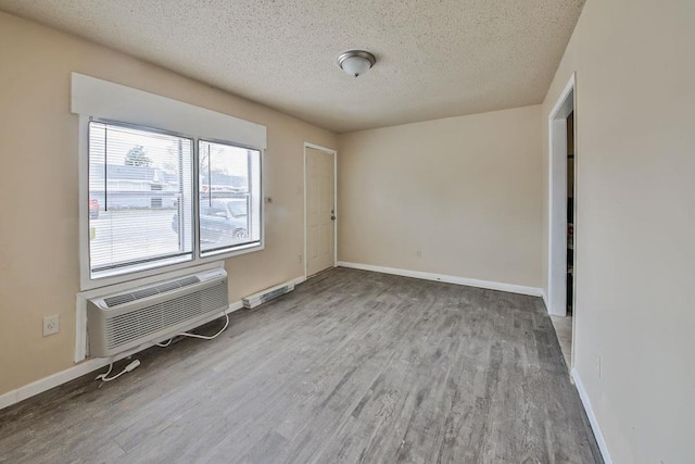 empty room featuring a textured ceiling, a wall mounted AC, and wood-type flooring