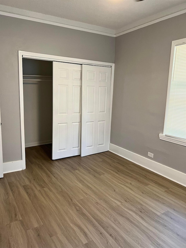 unfurnished bedroom featuring a closet, multiple windows, dark hardwood / wood-style floors, and ornamental molding