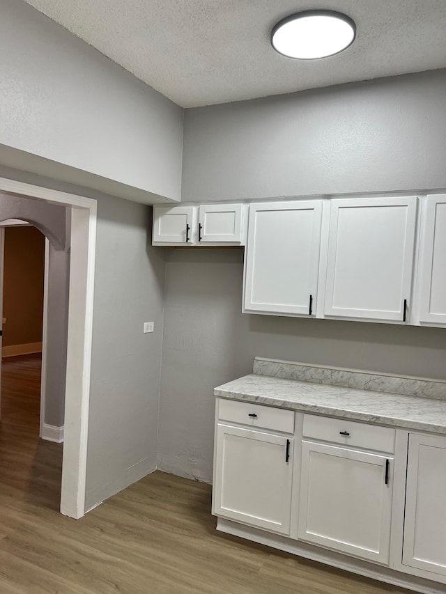 kitchen with a textured ceiling, light stone countertops, light hardwood / wood-style flooring, and white cabinetry