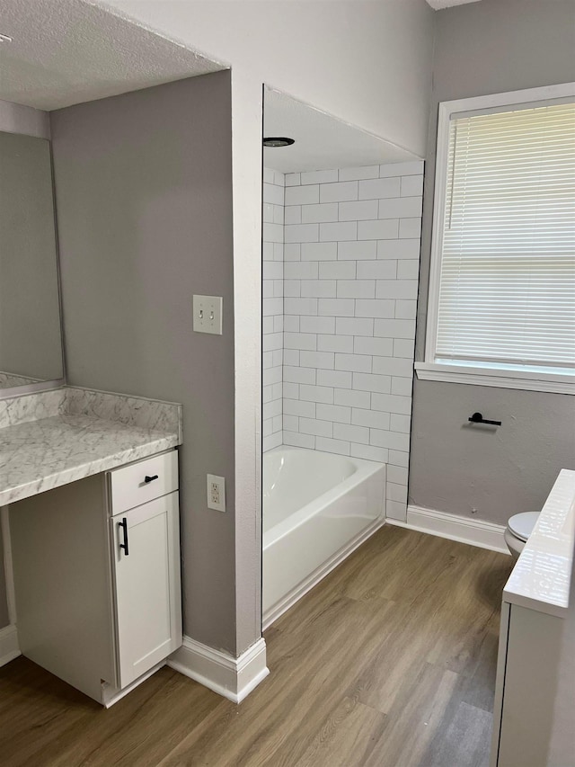 full bathroom featuring tiled shower / bath combo, vanity, wood-type flooring, a textured ceiling, and toilet